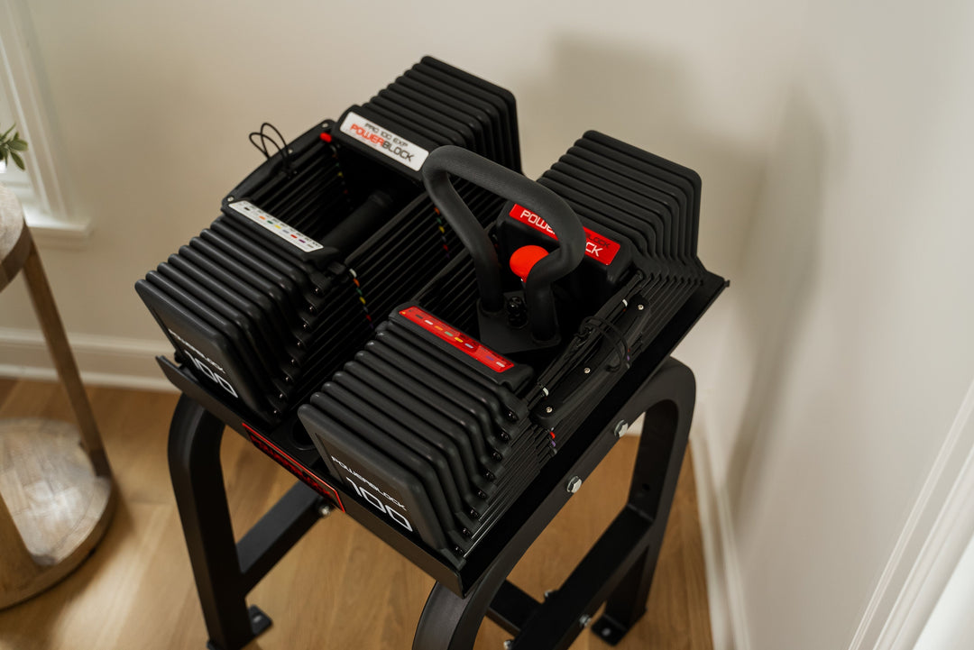 PowerBlock Pro 100 EXP Adjustable Dumbbell sitting on the Home Rack Stand, with one Dumbbell using the Pro 100 EXP Kettlebell handle.