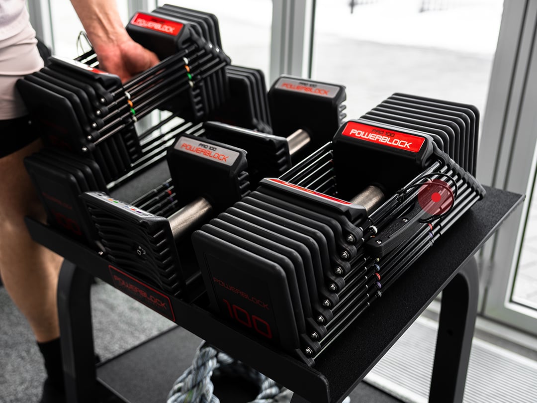 Man returning PowerBlock Commercial Pro 100 Adjustable Dumbbell to the Pro Rack Stand.