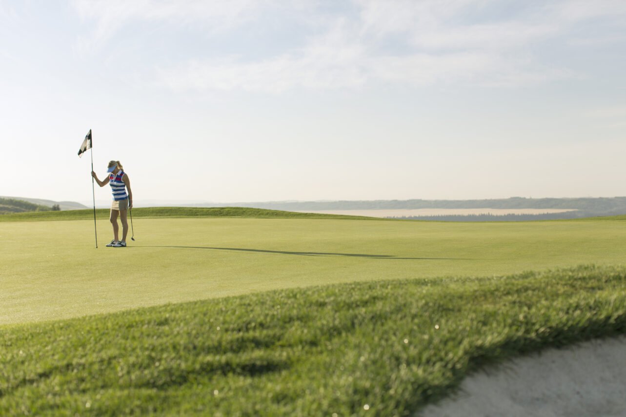 A woman on a golf course holds the flag, located on the green adjacent to the hole.