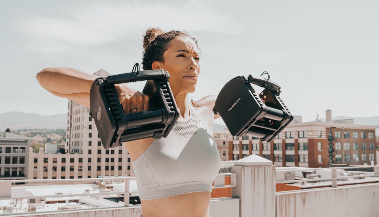 A woman works out on a rooftop, using PowerBlock adjustable dumbbells.