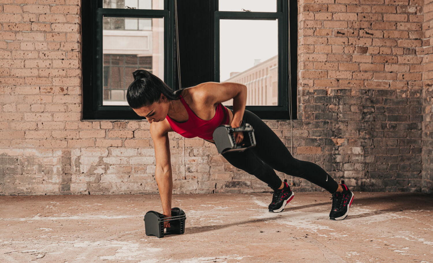 female athlete in an apartment performing a renegade row with adjustable dumbbells