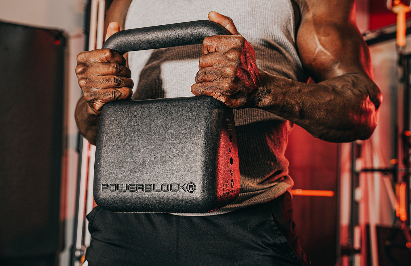 Tight image of a man in a sleeveless shirt holding a PowerBlock adjustable kettlebell.