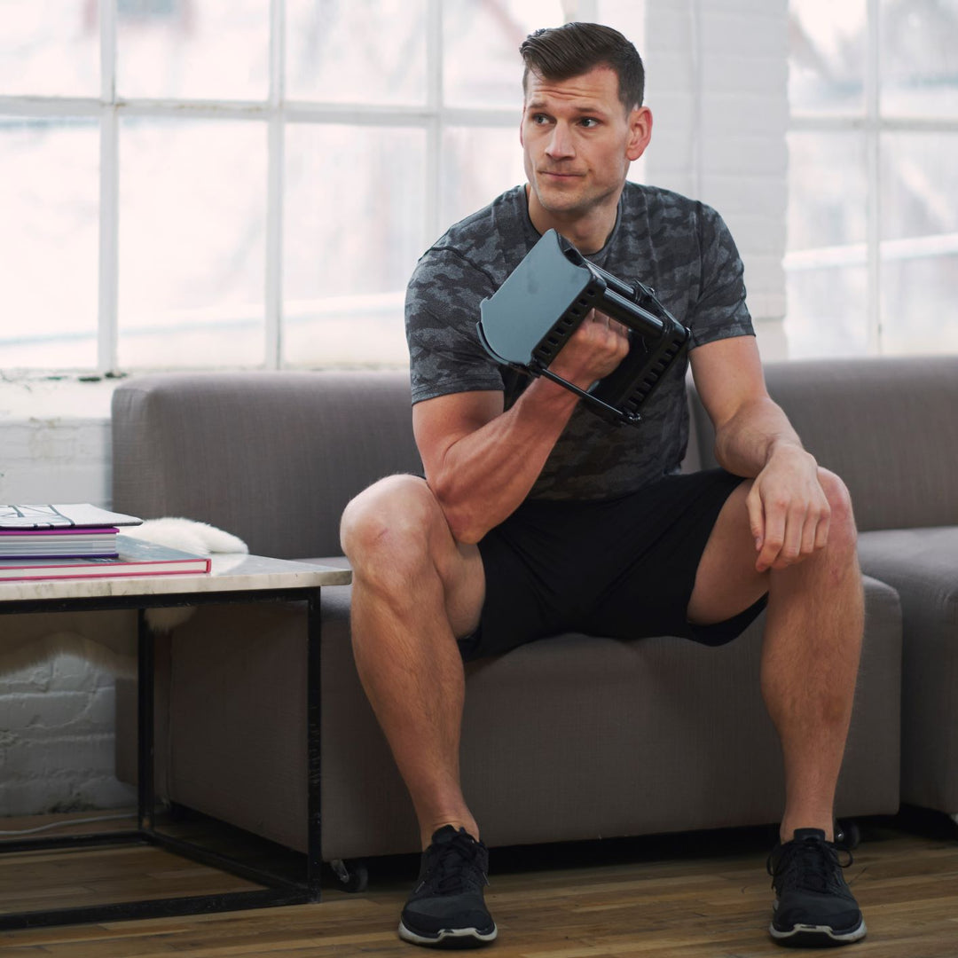 An athlete on a sofa looks uninterested as he does a curl with a PowerBlock adjustable dumbbell.