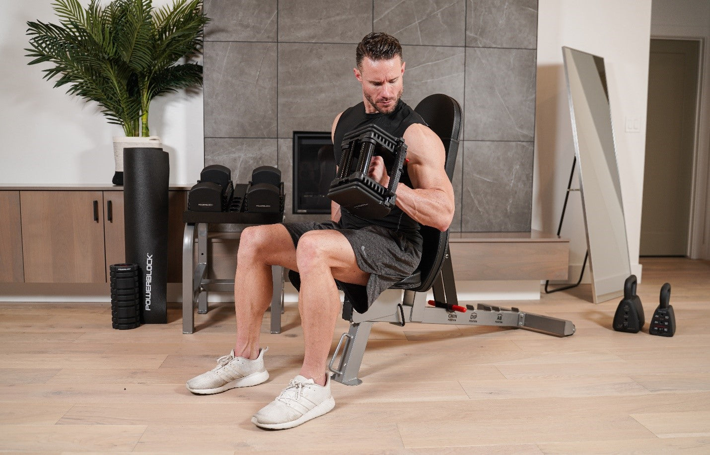 A male athlete with big arms curls PowerBlock adjustable dumbbells from a seated position.