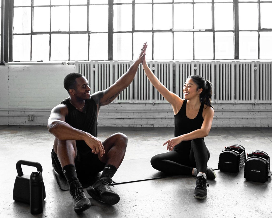 A man an woman give a high five after a dumbbell and kettlebell workout. 