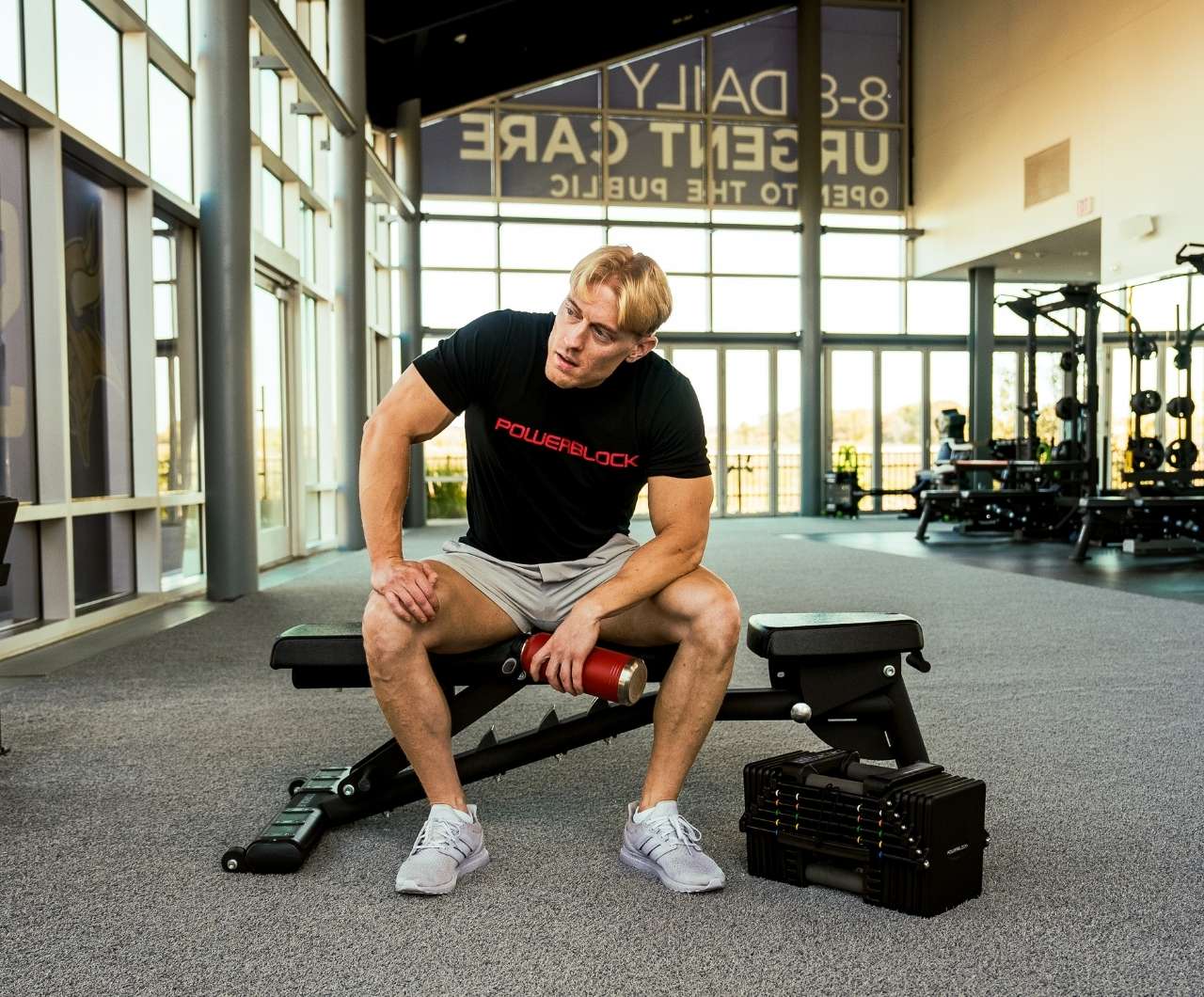 Man sitting on a bench next to a PowerBlock Commercial Pro 125/175 Adjustable Dumbbell