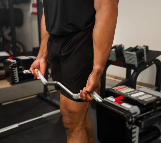 man in a low budget garage home gym holding an ez curl bar