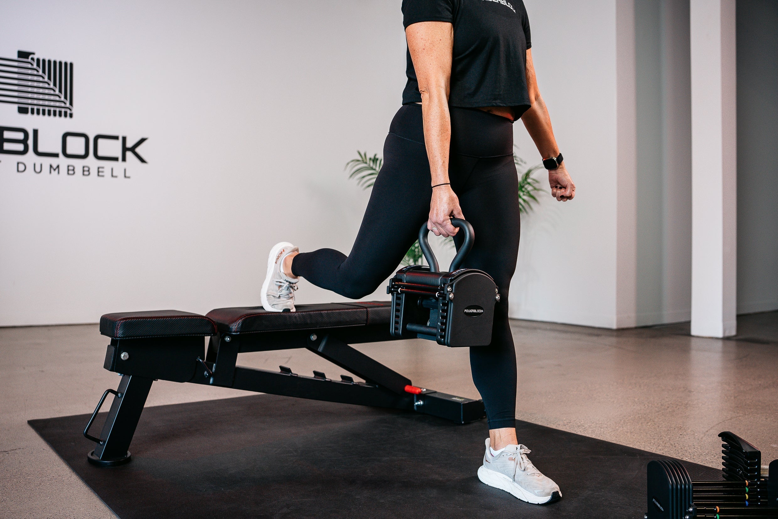 Woman performing a Bulgarian split squat using the PowerBlock Pro 50 Adjustable Dumbbell with the Pro Series Kettlebell Attachment