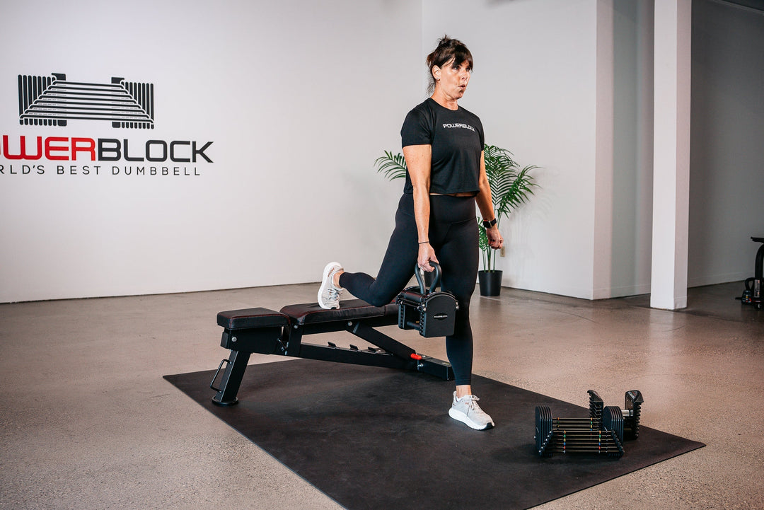 Woman using the PowerBlock Pro 50, Pro Series Kettlebell Handle, and PowerBench 2.0 to perform Bulgarian Split Squats