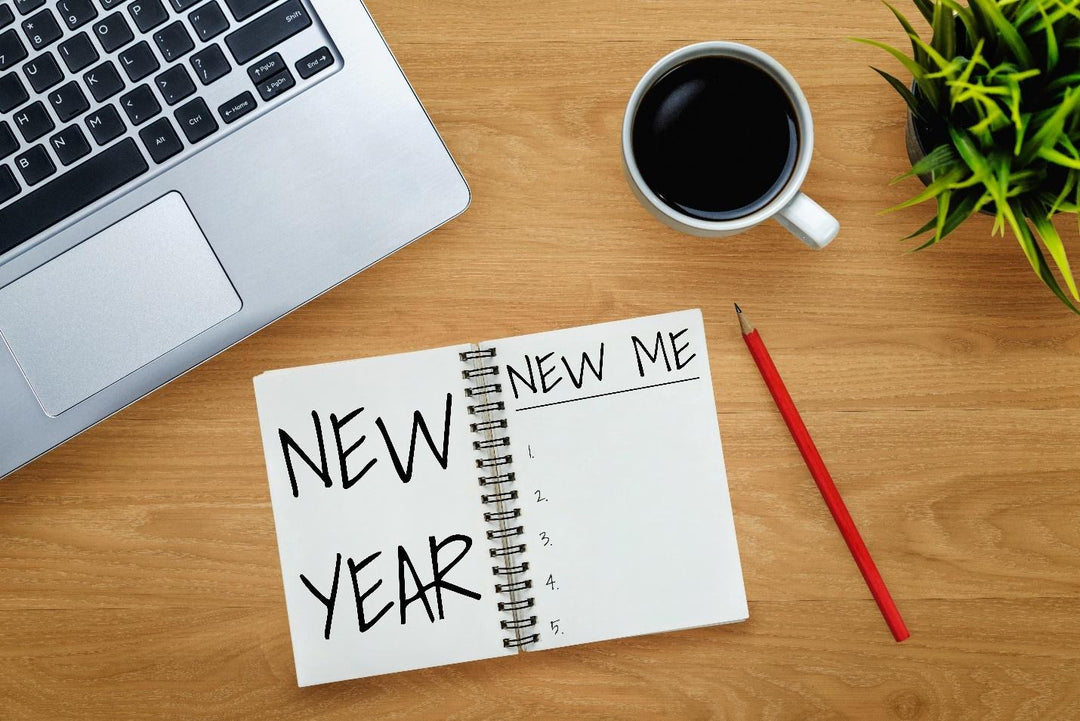 Desk with a laptop, coffee cup, pencil and notebook with "New Year" and "New Me" written inside.