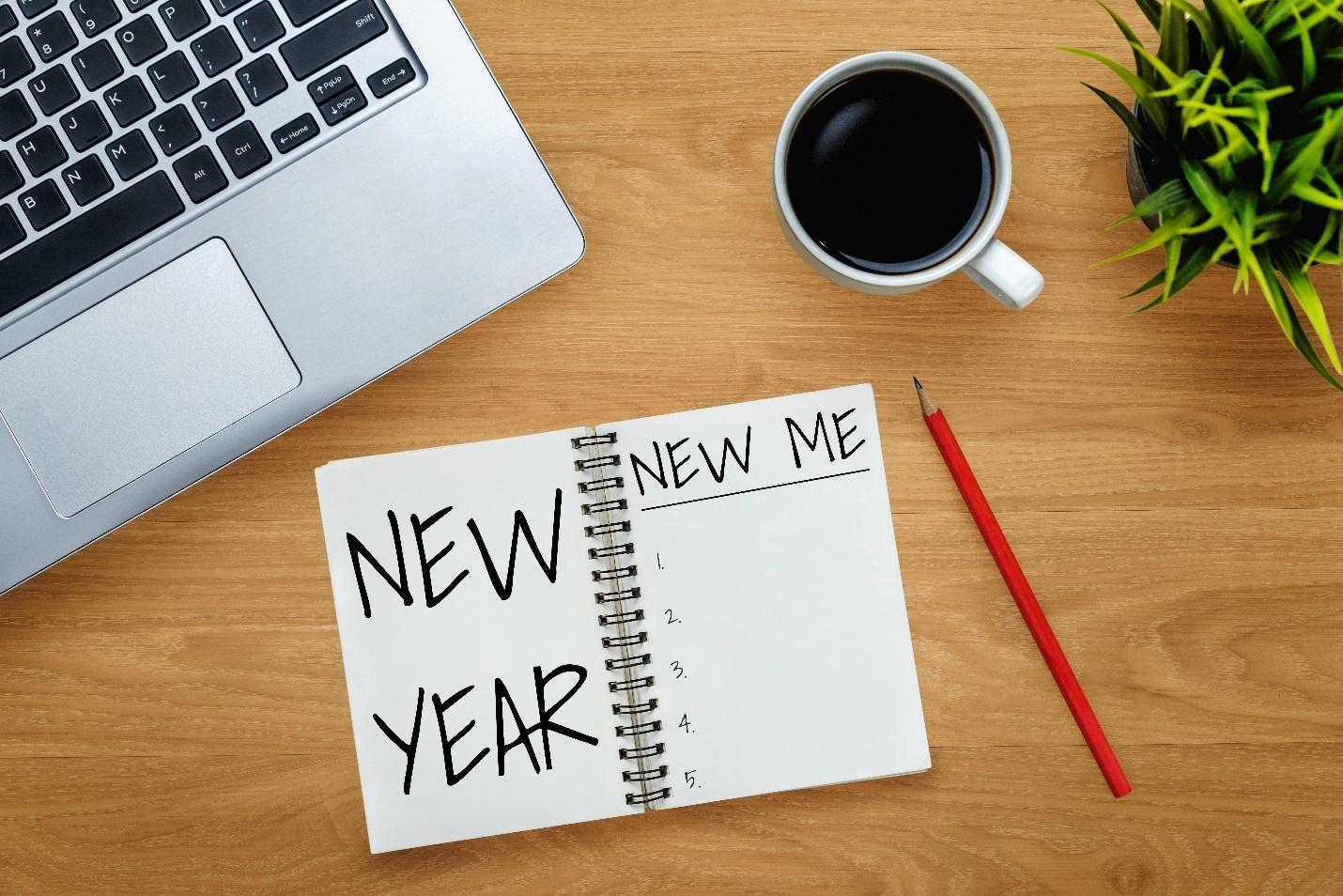 Desk with a laptop, coffee cup, pencil and notebook with "New Year" and "New Me" written inside.