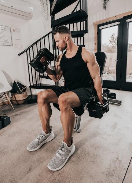 An athlete does seated curls with PowerBlock adjustable dumbbells in his home gym.