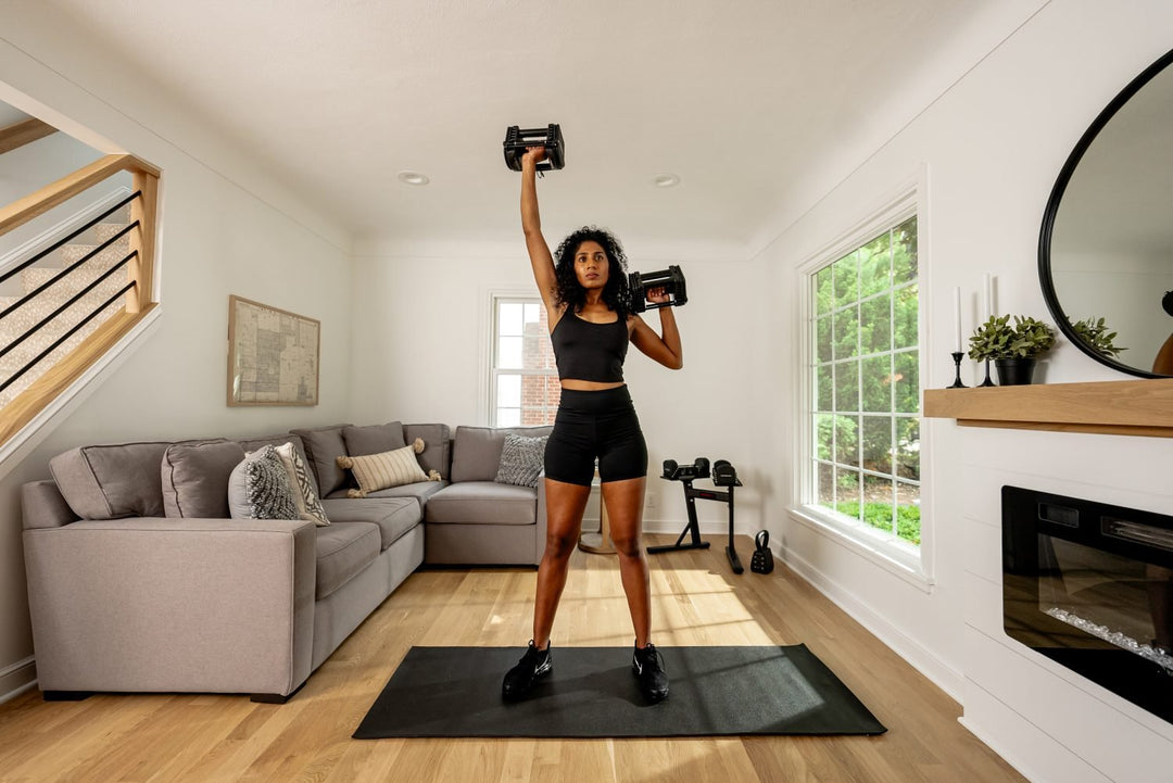 female athlete working out in a small living room home gym with powerblock adjustable dumbbells