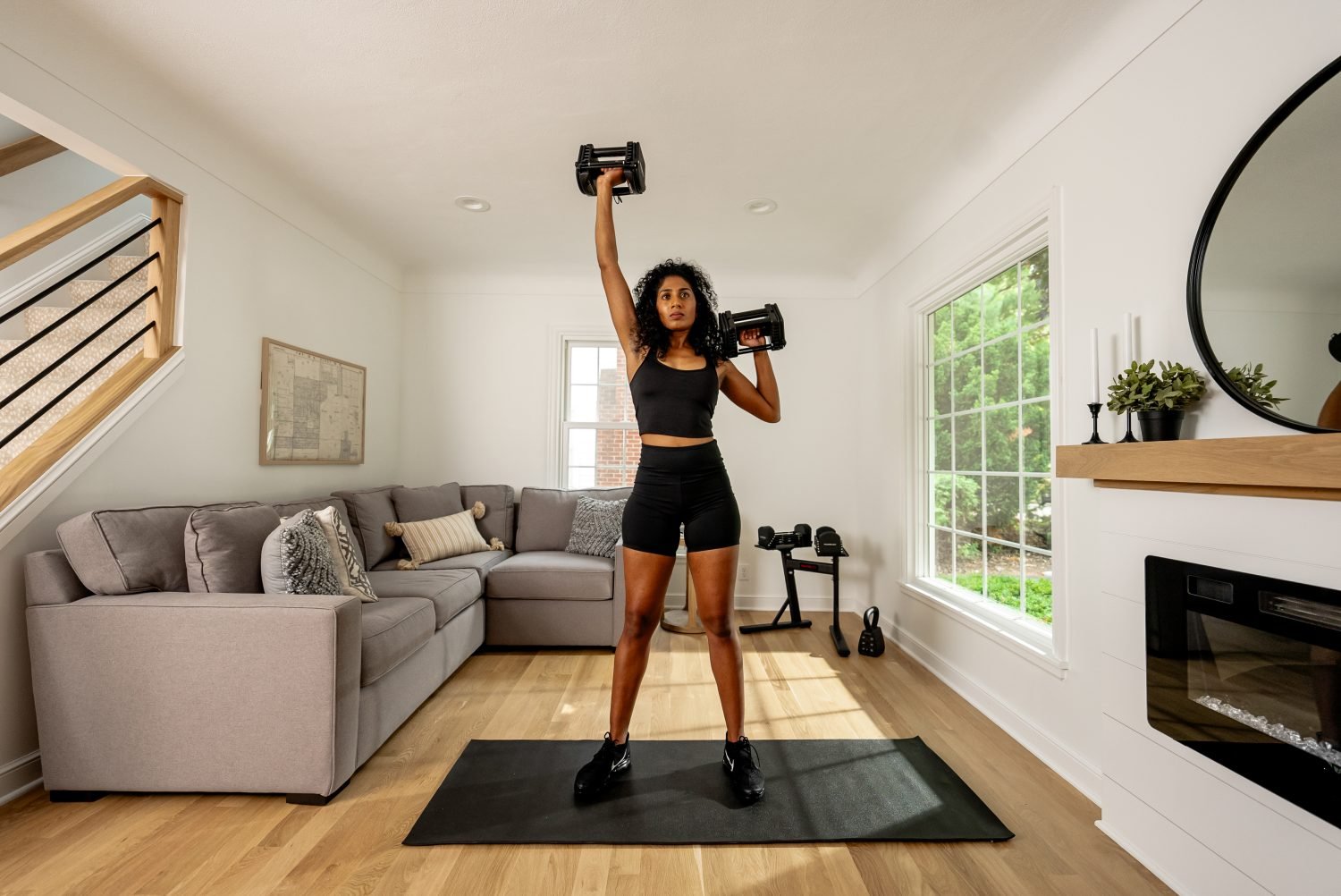 female athlete working out in a small living room home gym with powerblock adjustable dumbbells