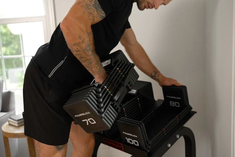 Fit man pulling PowerBlock adjustable dumbbells off of a stand to start a workout