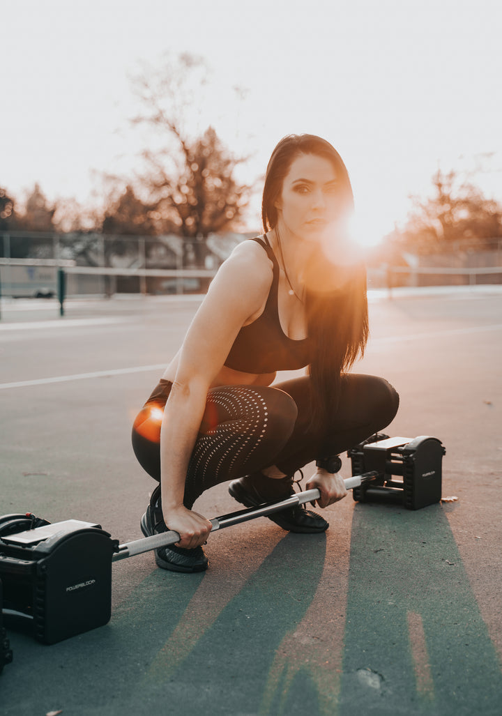 Woman next to PowerBlock Pro Series Straight Bar and Pro 50 Adjustable Dumbbells.