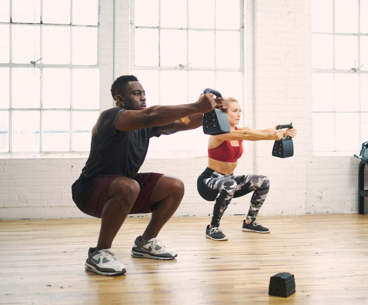man and woman in home gym squatting with heavy kettlebell