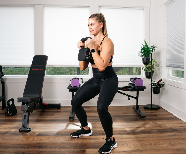 Woman in home gym doing kettlebell squats