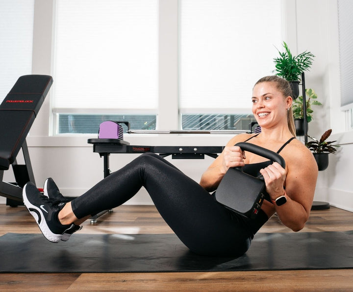 woman in home gym doing russian twists with light kettlebell