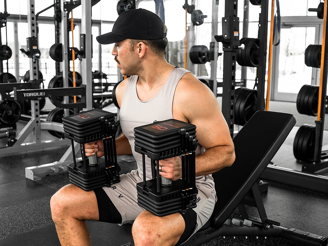 Man holding Commercial Pro 100 Adjustable Dumbbells with 50 lb weights.