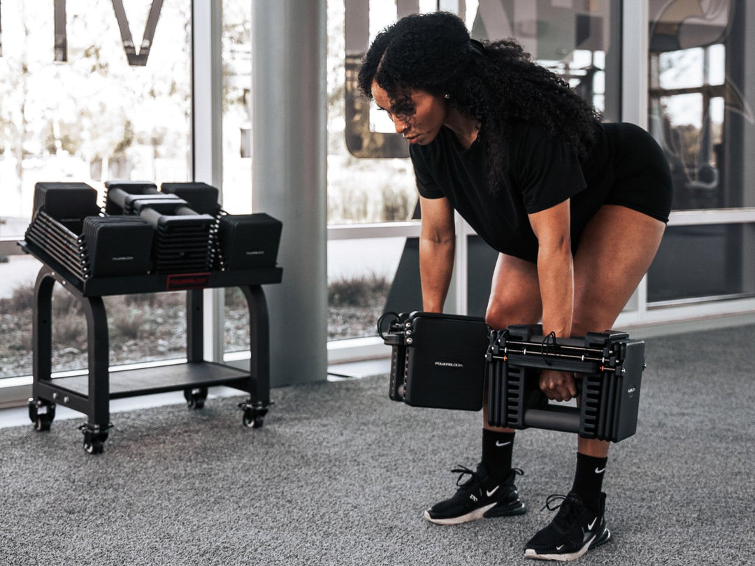 Woman doing a dead lift with Commercial Pro 175 Adjustable Dumbbells in background.