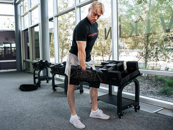 Man holding a PowerBlock Commercial Adjustable Dumbbell with the Pro Max Stand in background.