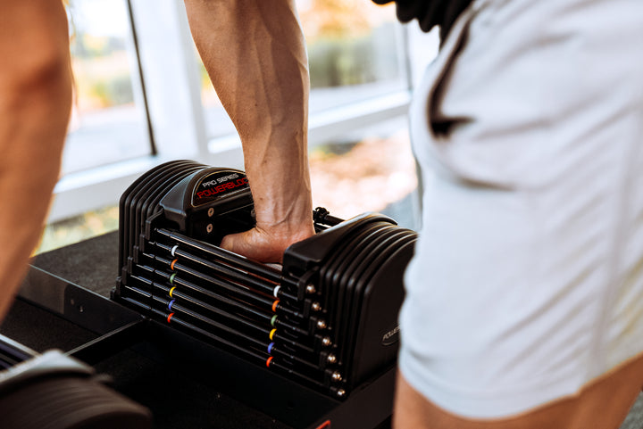 A close up of a man reaching for a PowerBlock Commercial Pro 50 Adjustable Dumbbell.