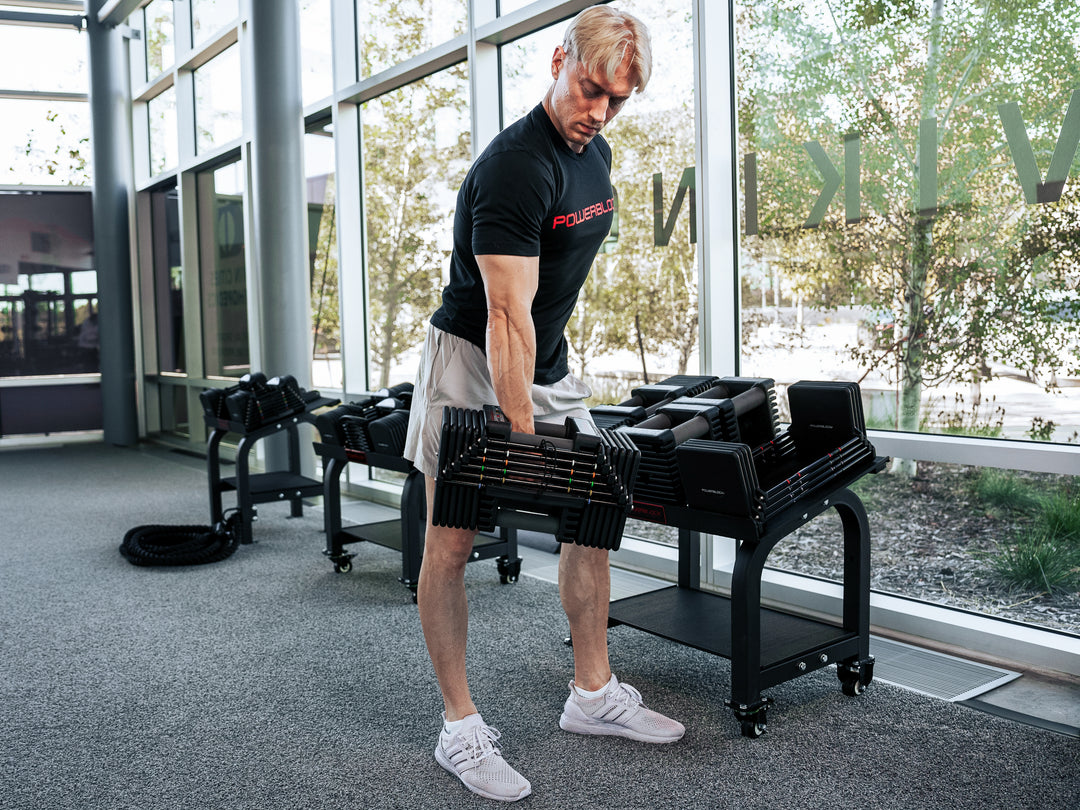 Man holding a PowerBlock Commercial Pro 125 Adjustable Dumbbell in front of a Pro Max Stand.