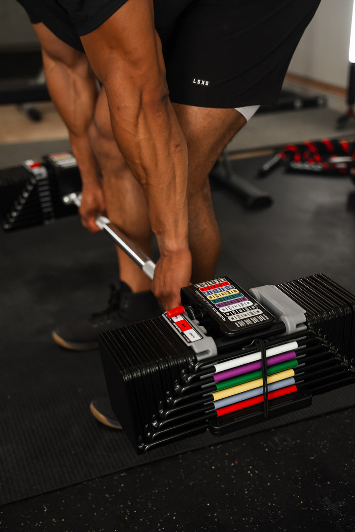 Man holding PowerBlock Elite USA Straight Bar and Elite USA 90 Adjustable Dumbbells with full weight stack.