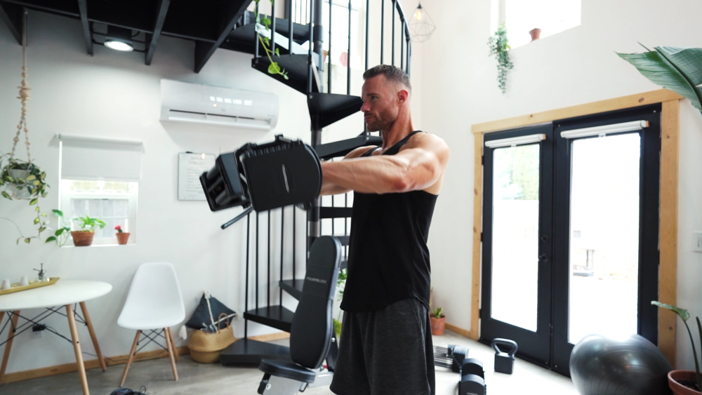 Side view of a man using two PowerBlock adjustable dumbbells for shoulder front raises