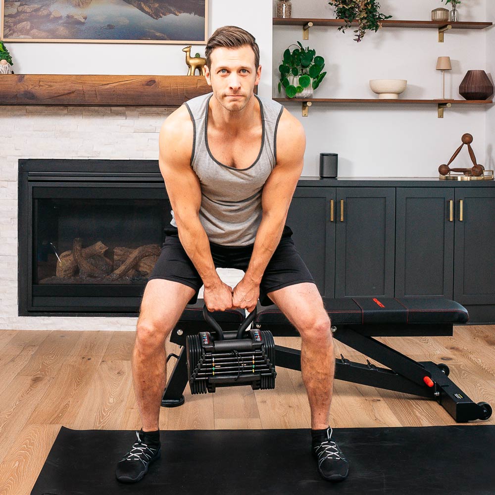 Male athlete using an adjustable dumbbell kettlebell handle attachment in a home gym