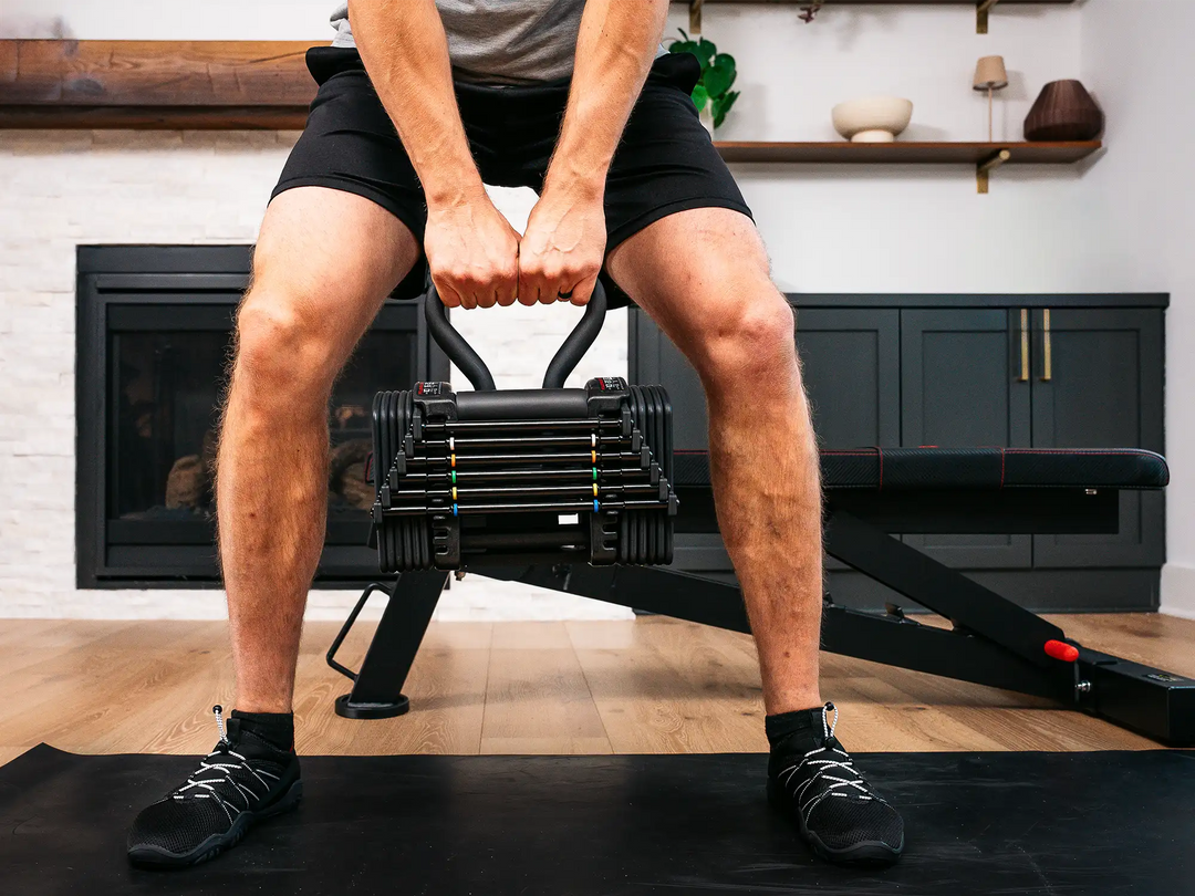 male athlete holding adjustable kettlebell with PowerBlock pro 50 adjustable dumbbell being used as a kettlebell.