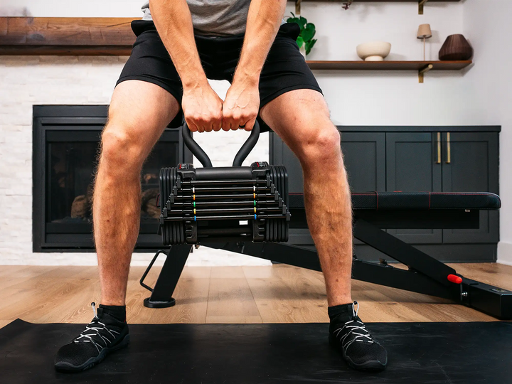 male athlete holding adjustable kettlebell with PowerBlock pro 50 adjustable dumbbell being used as a kettlebell.