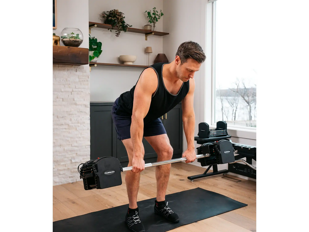Male athlete using a PowerBlock Pro Series Straight Bar adjustable barbell with 50 pound adjustable dumbbells.