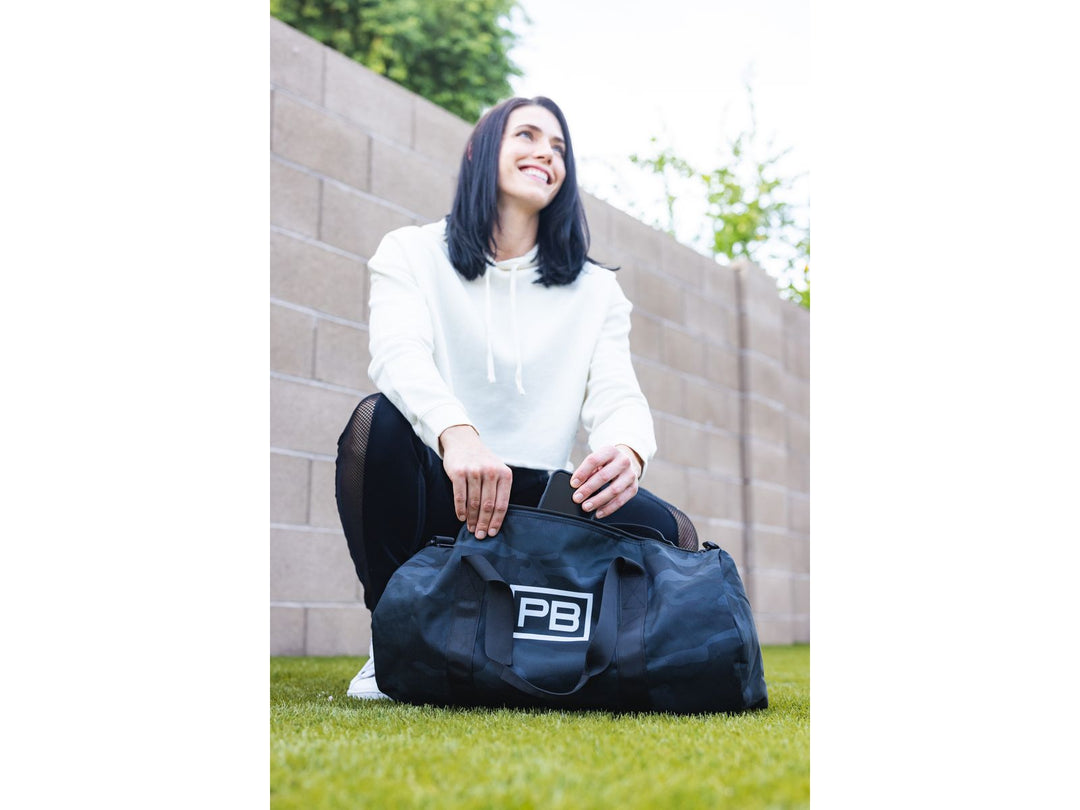 Woman kneeling to close black PowerBlock Duffle Bag on the ground.