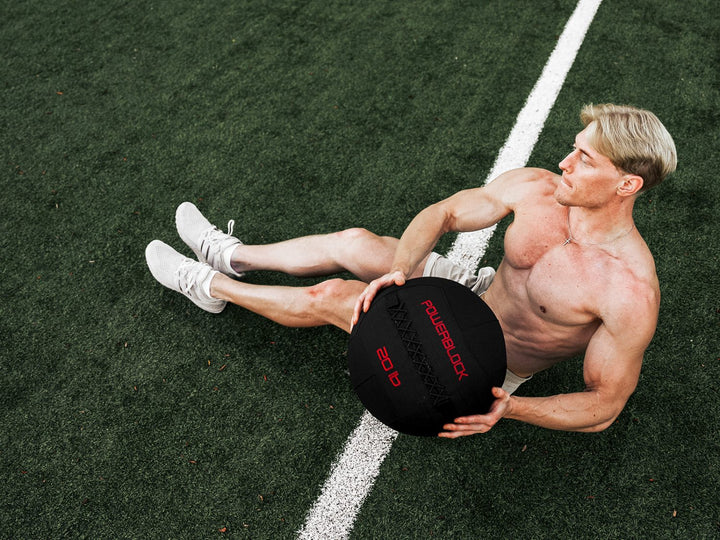 shirtless athlete on athletic field doing a russian twist with a PowerBlock wall ball