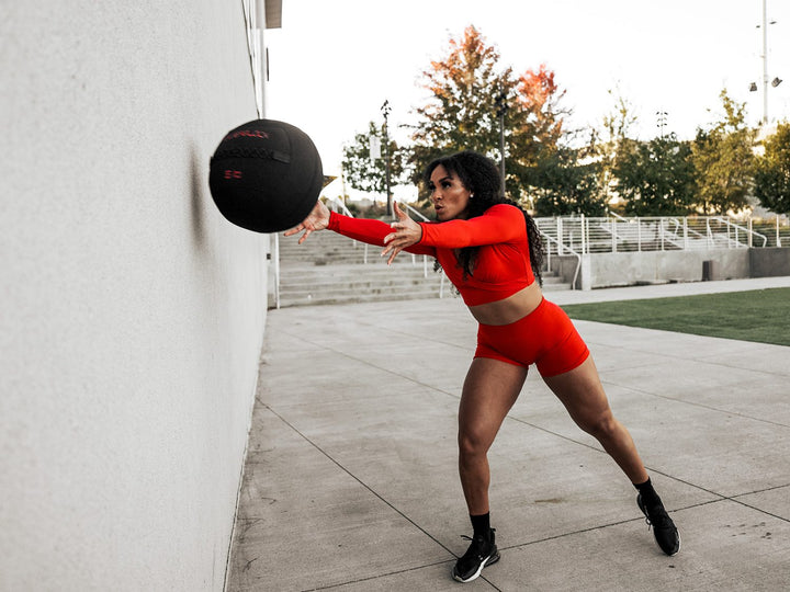 Female athlete throwing a large 5 pound ballistic grade medicine ball at a concrete wall