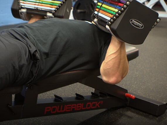 An athlete does bench presses with adjustable dumbbells while on the PowerBlock PowerBench.
