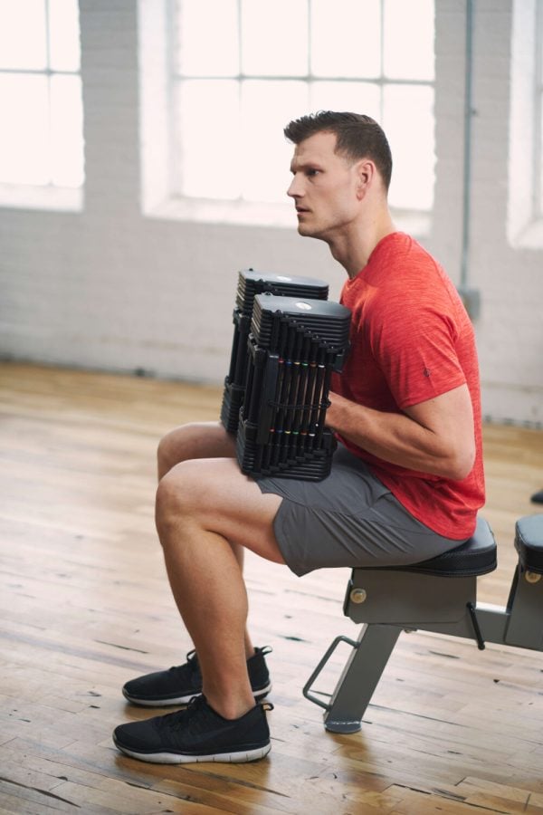 An athlete sits on his workout bench, between sets of curls with his Pro 50 adjustable dumbbells.
