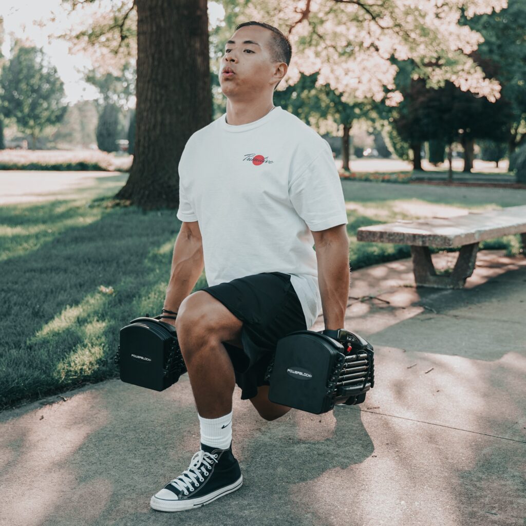 An athlete in the park takes a breath as he works out using PowerBlock adjustable dumbbells.