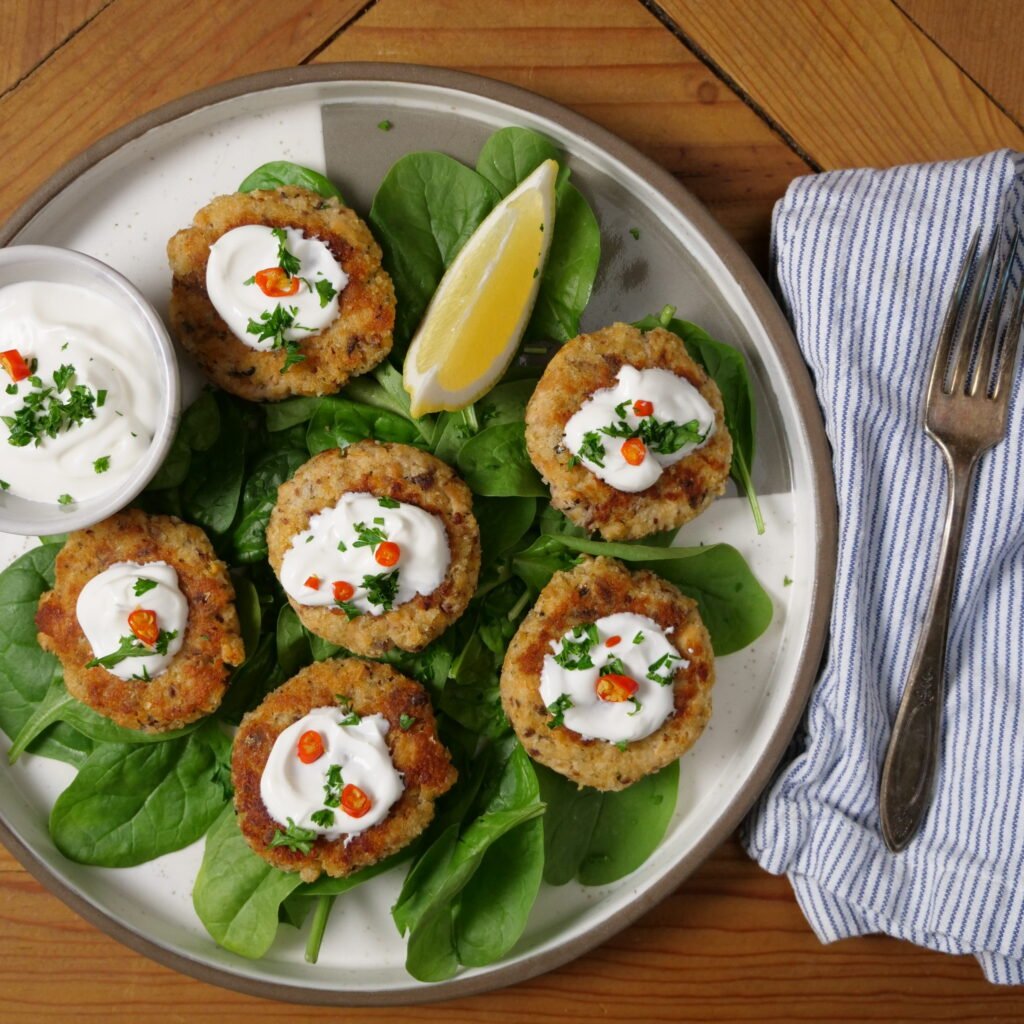 Plated Healthy Salmon Patties on a bed of lettuce with a lime wedge and a cup of sour cream.