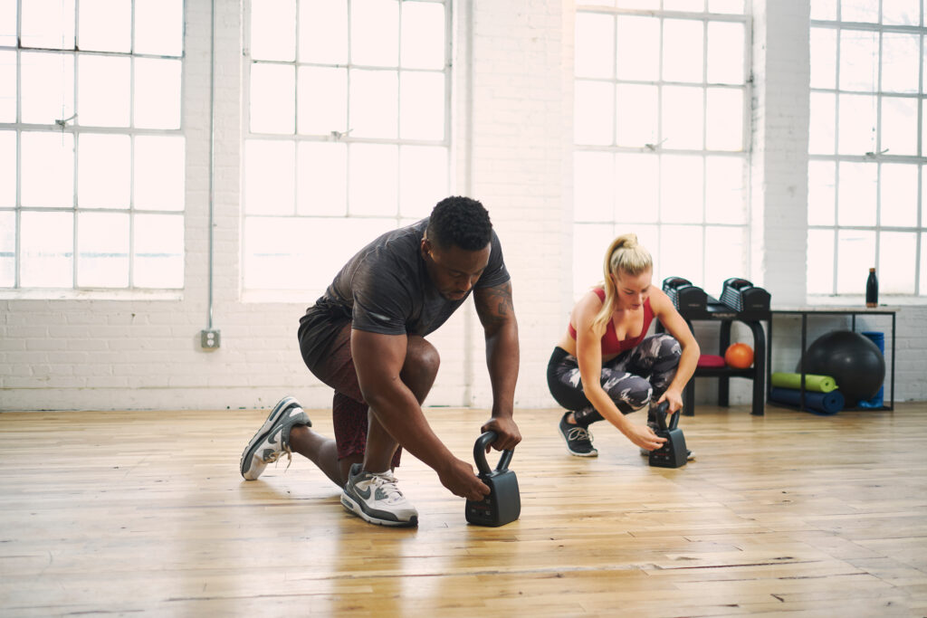 Two athletes, a male and a female, work out in a studio using PowerBlock kettlebells.