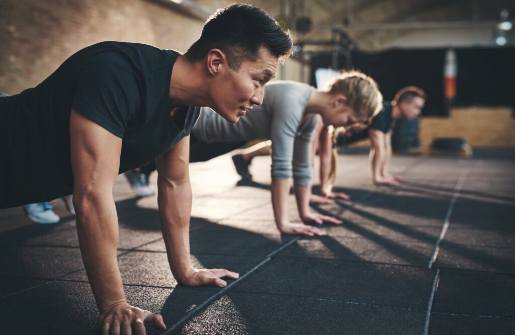 Line of four people holding a plank pose and watching an unseen instructor or timer.