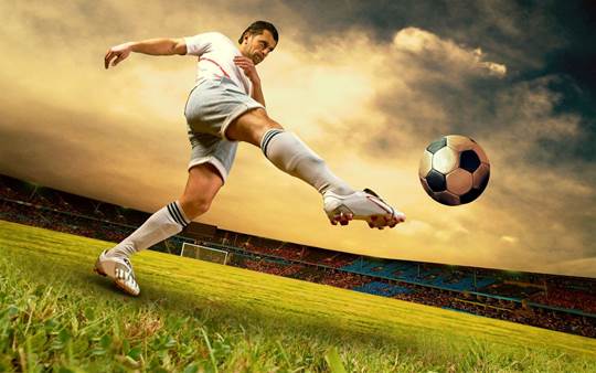 An athlete in a stadium on a cloudy day kicks a soccer ball downfield.