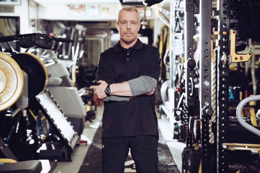 Trainer Gunnar Peterson standing in is professional gym, crossing his arms