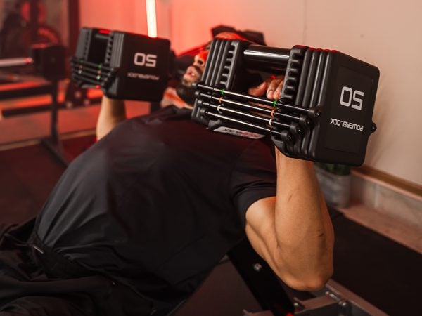 man using 50 pound adjustable dumbbells to perform a chest press in a home gym